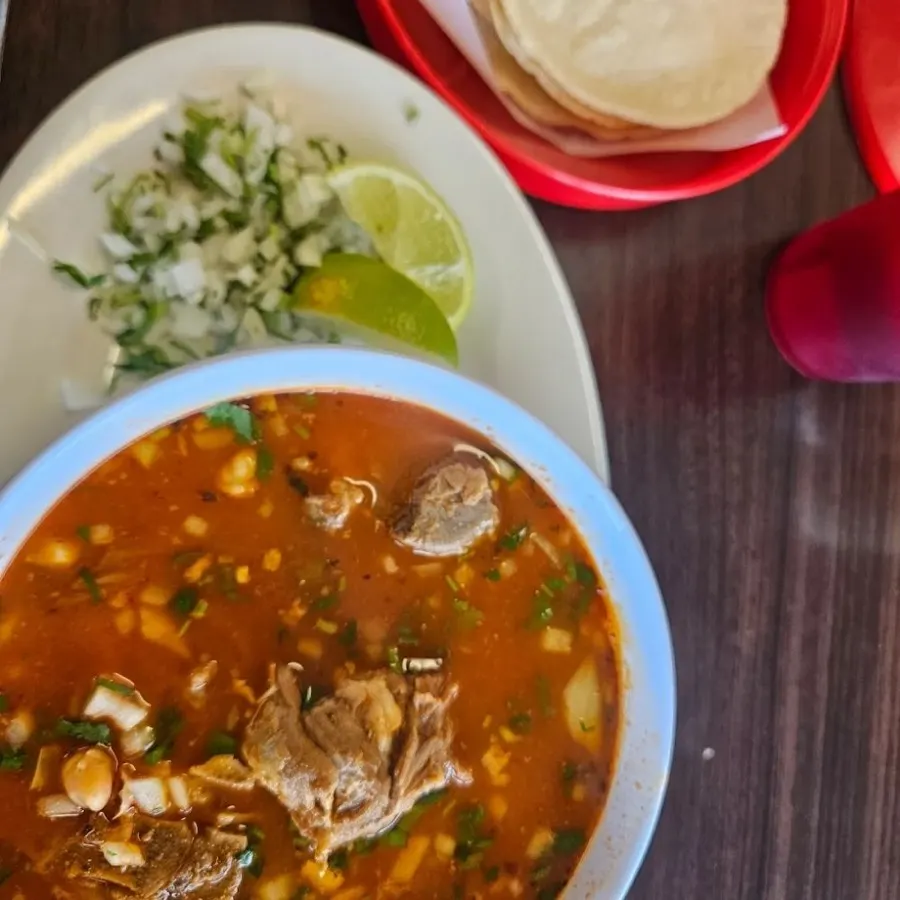 Bowl of menudo with fresh corn tortillas, onion, cilantro and lime